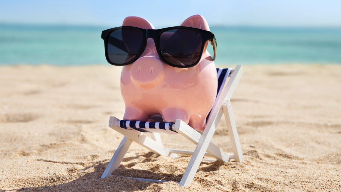 Foto de um cofre de porquinho usando óculos de sol na praia