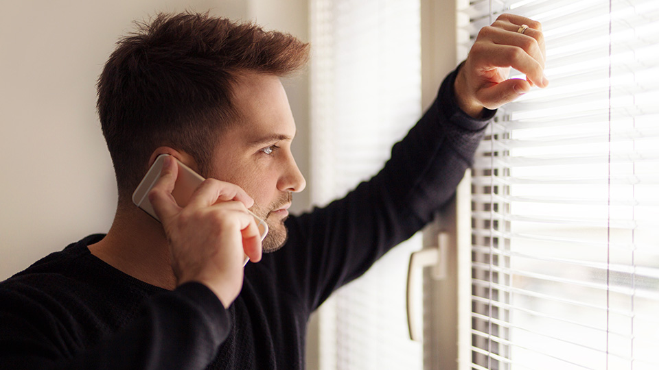 Foto de homem falando no telefone e olhando pela janela.